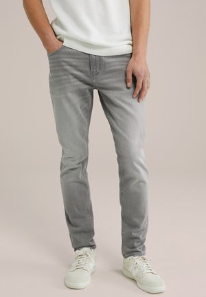 Vaaleanharmaat farkut slim fit -leikkauksella, viidellä taskulla ja haalistuneella pinnalla, yhdistettynä valkoisiin lenkkareihin.