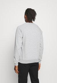 Sweat-shirt gris avec col rond et poignets côtelés, présentant un design simple et une texture douce, associé à un pantalon noir.