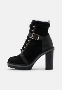 Černé kotníkové boty vyrobené z semiše a kůže, s kožešinovým lemem, zlatými očky, přezkou, výrazným podpatkem a strukturovanou podrážkou.
