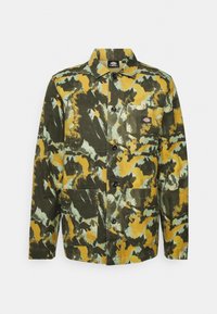 Grön, gul och blå kamouflagemönstrad jacka med krage, knappstängning och två framfickor. Hållbar tygstruktur synlig.