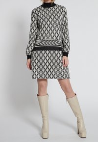 Abito a righe bianco e nero con maniche lunghe, colletto alto e una vita a righe; abbinato a stivali beige con tacco al ginocchio.