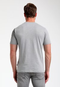 Harmaa t-paita, jossa on lyhyet hihat ja olkapäissä teksturoitu, geometrinen kuvio. Kiva kangas ja rento malli.