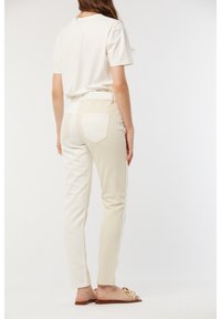 T-shirt blanc associé à un pantalon droit beige clair, comportant deux poches arrière et un motif ondulé subtil sur le détail des poches.