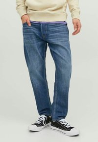 Blå denimjeans med rak passform, med subtila slitningar och femfickdesign, i kombination med svarta och vita kanvas sneakers.