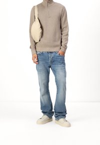 Beige zip-up trui, blauwe denim jeans, crèmekleurige sneakers en een beige schoudertas. Casual look met een ontspannen ontwerp en textuur.