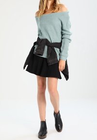 Suéter de punto azul claro con hombros al aire, falda skater negra y botines negros. Chaqueta oscura atada a la cintura que añade detalle. Look simple y casual.