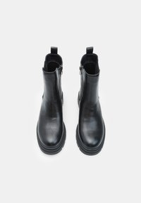 Melni ādas potītes zābaki ar gludu apdari, sānu rāvējslēdzējiem un masīvu gumijas zoli. Dizains izceļas ar minimālistisku, slaidu formu.