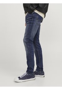 Tmavě modré džínsy slim fit vyrobené z denimu s vybledlými částmi, doplněné černou bundou a námořnickými teniskami s bílou podrážkou.