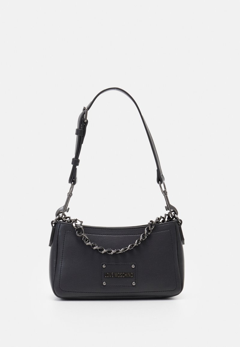 Sac à main en similicuir noir avec une silhouette courbée, des accents en chaîne et sangle, et une plaque logo métallique à l'avant.