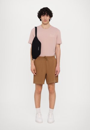 Lyserød kortærmet t-shirt, brune shorts med snoretræk, sort crossbody taske, hvide sneakers og hvide ankelstrømper. Enkel, afslappet outfit.