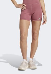 Tætsiddende pink atletikshorts lavet af strækbart materiale med en glat tekstur, prydet med hvide logoakcenter på venstre side.