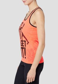Top deportivo de color coral brillante con acentos negros y un texto gráfico audaz. Presenta tirantes finos y un diseño ajustado para el uso activo.