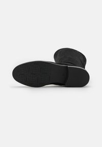 Black suede ankle boot with a rounded toe and a flat sole. The underside features an embossed logo pattern and minimal tread design.