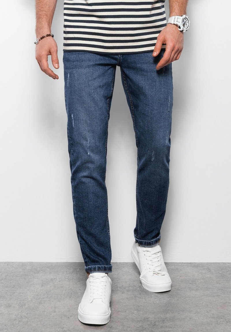 Jeans en denim bleu foncé ajustés, avec des dégradés subtils et des détails vieillis. Assortis à des baskets blanches et un haut rayé.