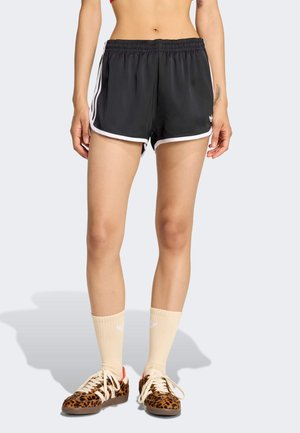 Czarne sportowe szorty z białymi akcentami, elastycznym paskiem w talii i gładką fakturą. Noszone z butami w panterkę i kremowymi skarpetkami.