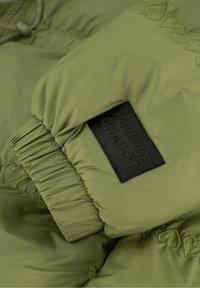 Olijfgroene pufferjack met details van gathered elastische manchetten, voorzien van een zwart stoffen label met de opdruk "Fabienne Chapot" en hart borduursel.