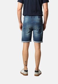 Shorts en denim avec des retroussages, délavage bleu clair à moyen, design à cinq poches et décoloration subtile. Baskets blanches avec des accents noirs.
