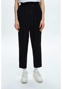 Svarta byxor med hög midja, avslappnad passform och veck fram. Har dragsko i midjan och sidofickor. Bärs med vita sneakers.