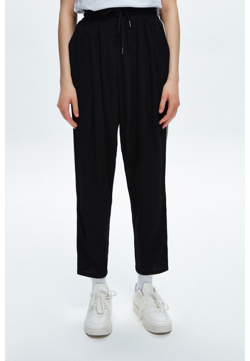 Svarta byxor med hög midja, avslappnad passform och veck fram. Har dragsko i midjan och sidofickor. Bärs med vita sneakers.