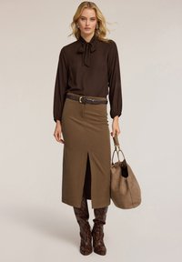 Blusa marrón con pajarita, falda verde olivo con abertura en la parte delantera, cinturón marrón, botas de serpiente hasta la rodilla, y un bolso suave marrón.