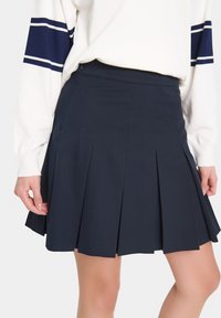 Fustă plisată bleumarin cu talie ajustată și textură netedă. Prezintă plisuri ascuțite și o margine curată, potrivită pentru ținute casual sau semi-formale.