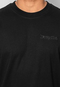 Sort bomulds T-shirt med rund halsudskæring og en blød tekstur, med "Dropsize" broderet i en mørk, dekorativ skrifttype på brystet.