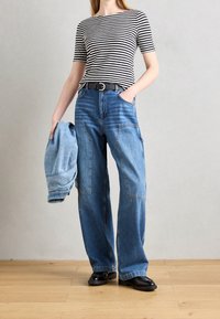 Camisa de manga corta a rayas, vaqueros de pierna ancha azules con bolsillos, cinturón negro y chaqueta vaquera sostenida en una mano. Textura suave y diseño casual.