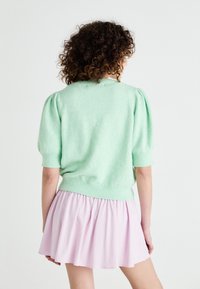 Mintgrön stickad tröja med korta puffärmar, kombinerad med en ljusrosa utsvängd kjol. Mjuk textur med ribbad kantdetalj.