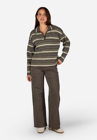 Dryžuotas megztinis žalių ir smėlio spalvų atspalviais, turi apykaklę ir pusiau užtrauktuką. Pora su šviesiai rudiomis plėšytomis kelnėmis ir smėlio spalvos bateliais.