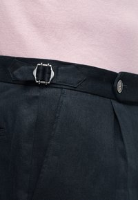 Μαύρη ζώνη μέσης με ρυθμιζόμενη ασημένια αγκράφα και κουμπί σε σκούρο παντελόνι, φορεμένη με ανοιχτό ροζ τοπ.