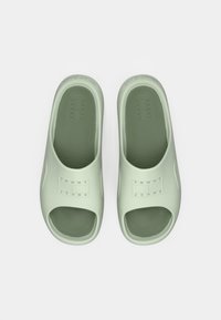 Une paire de slides ouvertes de couleur vert clair avec "Tommy Jeans" embossé sur la sangle, vues de dessus sur un fond blanc.
