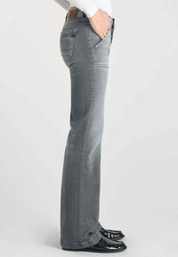 Jean en denim gris avec une coupe droite, présentant des coutures contrastées, des poches arrière et une texture lisse. Portés avec des chaussures noires.