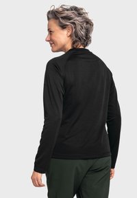 Schwarzes Langarmshirt mit runden Ausschnitt und Raglanärmeln, mit einer glatten Textur. Getragen mit grünen Hosen.