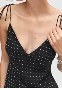 Robe noire à pois avec un décolleté en V, des fines bretelles et une texture douce et soyeuse. Présente un design croisé à l'avant.