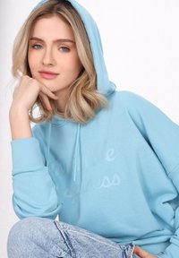 Sudadera azul clara hecha de una tela suave, con un corte holgado, cordones y el texto "Felicidad Invisible" en una impresión sutil.