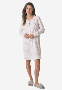 Pitkähihainen valkoinen yöpaita, jossa on hentoinen kukkakuvio, pyöreä pääntie napillisen aukon kanssa ja pehmeä kangaspinta.