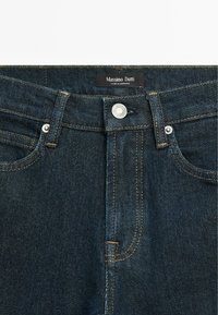 Jean en denim bleu foncé avec surpiqûres orange, fermeture par bouton argenté, deux poches avant et étiquette "Massimo Dutti" sur la ceinture.