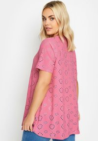 Top de manga corta rosa con diseño calado que presenta formas de corazones y círculos. Textura suave y corte relajado, combinado con denim azul.
