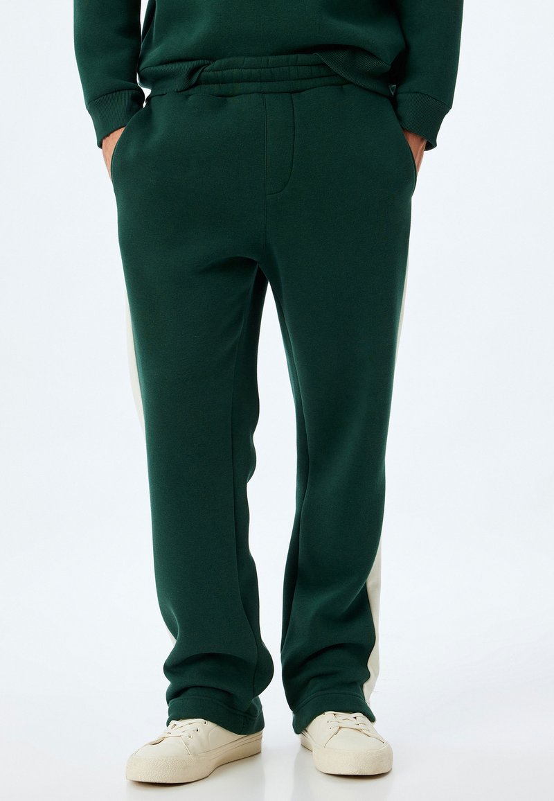 Pantalones de chándal verdes con un ajuste relajado, que cuentan con bolsillos laterales y paneles laterales blancos. Hechos de una tela suave y elástica para mayor comodidad.