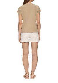 Beige top met korte mouwen van zachte stof, gecombineerd met witte denim shorts. Model draagt lichtgekleurde sandalen. Eenvoudig ontwerp, geen patronen.