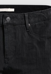 Vaqueros negros de mezclilla con corte recto, que cuentan con trabillas para cinturón, bragueta con cierre de cremallera y botón, y una textura sutil.