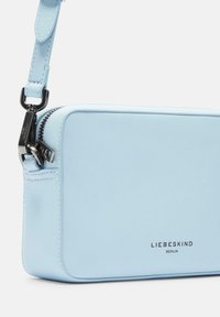 Jasnoniebieska syntetyczna torebka w kształcie prostokąta, z zamknięciem na zamek i czarnymi elementami metalowymi; posiada wytłoczone logo z przodu.