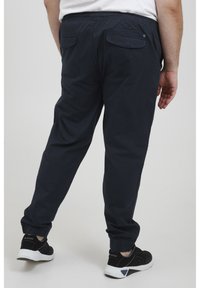 Marine joggingsbroek met elastische tailleband en ribgebreide boorden, met twee achterzakken en een gladde textuur. Gekleed met zwarte sneakers.