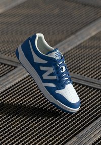 Sapatilha azul e branca com um superior texturizado, bico perfurado e logótipo "N" em destaque. Apresenta atacadores combinados e colarinho almofadado.