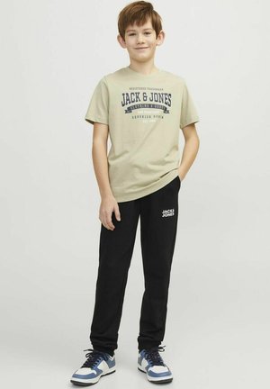 Ljusgrön t-shirt med marinblå tryckt logotyp, kombinerad med svarta sweatpants med en vit logotyp. Sneakers med blå och vita detaljer.