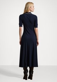 Ναυτικό πόλο φόρεμα με κοντά μανίκια, εφαρμοστό κορσάζ και ροή φούστας. Κατασκευασμένο από απαλό, ελαστικό ύφασμα, με γιακά και χρυσές λεπτομέρειες.