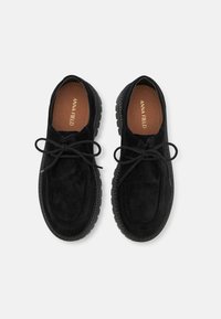 Scarpe in suede nero con punte tonde, stringhe piatte nere e suole in gomma testurizzata. Nome del marchio in oro stampato sulle solette marroni.
