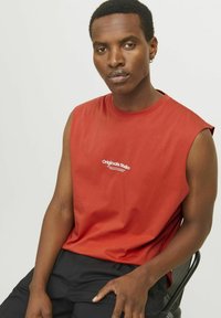 Rød ærmeløs T-shirt lavet af jersey materiale, med hvid logo-tekst "Originals Studio" på forsiden. Glat tekstur.