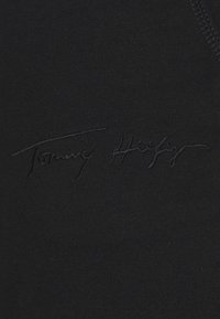 Schwarzer Baumwollstoff mit einer tonal geprägten Signatur "Tommy Hilfiger", die dem glatten Inhalt eine strukturierte Note verleiht.