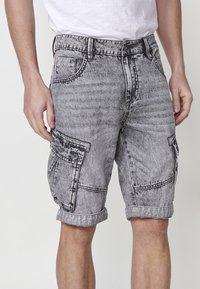 Shorts cargo en denim gris avec un motif décoloré, dotés de grandes poches latérales, d'un ourlet roulé et de passants de ceinture traditionnels.